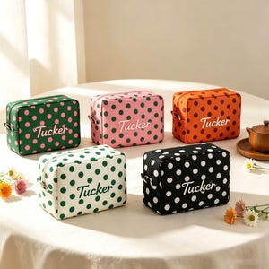 May include: Five rectangular toiletry bags featuring a polka dot pattern and the name Tucker embroidered on the front. The bags come in green with pink dots, pink with green dots, orange with brown dots, white with green dots, and black with white dots.