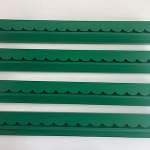 May include: Four identical long, narrow green shelves arranged horizontally. Each shelf features a decorative scalloped edge along the top front and a flat, straight base, providing a consistent profile for wall-mounted display or storage.