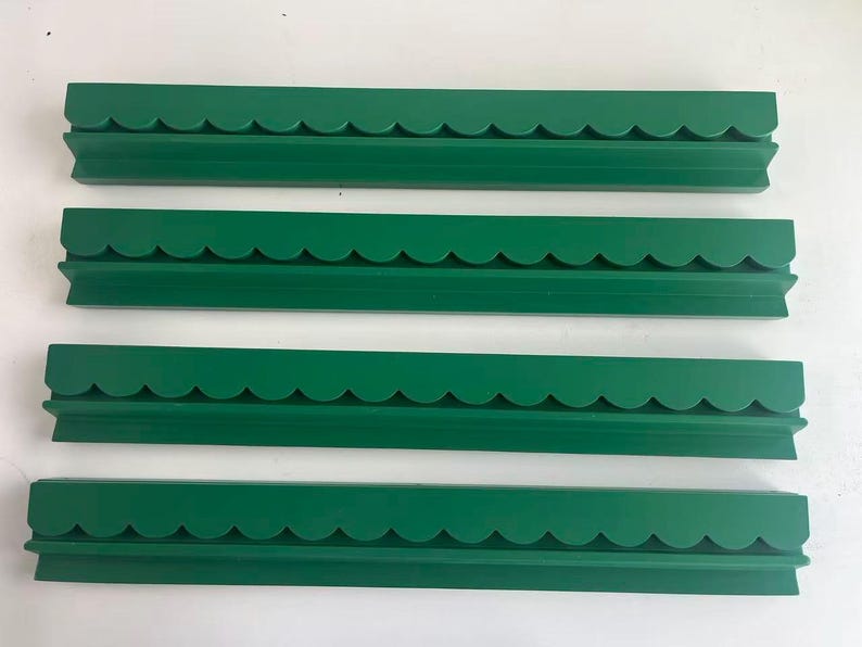 May include: Four identical long, narrow green shelves arranged horizontally. Each shelf features a decorative scalloped edge along the top front and a flat, straight base, providing a consistent profile for wall-mounted display or storage.