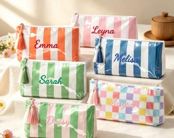 May include: Five rectangular zippered pouches with tassels. One is orange and white striped with 'Emma', one pink and white with 'Leyna', one blue and white with 'Melisa', one green and white with 'Sarah', one green and pink striped with 'Daisy', and one checkered with 'Aayra'.