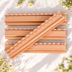 May include: Four peach-colored wall-mounted shelves arranged in a stack. Each shelf features a scalloped top edge and a flat horizontal surface with small circular screw holes visible along the front face of the shelf structure.