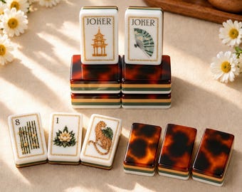 May include: A set of rectangular Mahjong tiles featuring white faces with gold-toned illustrations of a pagoda, a fan, bamboo, a lotus, and a leopard. The tiles have tortoiseshell-patterned backs and layered green, white, and gold bases.