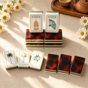 Könnte beinhalten: Ein Set rechteckiger Mahjong-Spielsteine mit weißen Vorderseiten, die eine Pagode, einen Fächer, eine Palme, eine Lotusblüte und ein Seerosenblatt zeigen. Die Steine haben eine Rückseite in Schildpattoptik und geschichtete grüne, weiße und braune Ränder.