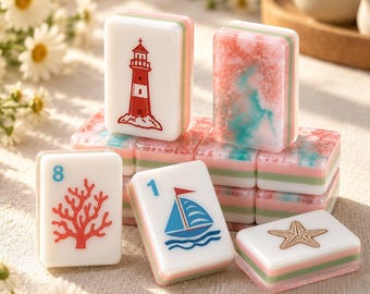 May include: A collection of rectangular mahjong tiles featuring nautical designs including a red lighthouse, a blue sailboat, a red coral branch, and a gold starfish. Some tiles have a pink and teal marbled pattern, with layered white, green, and pink sides.