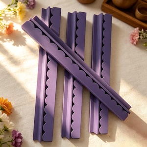 May include: Four long, purple, rigid strips with a scalloped edge along one side. These linear objects feature a flat base and a raised, decorative border with a repeating semi-circular pattern, arranged in a parallel and overlapping formation.