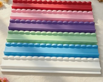 May include: A set of six rectangular wall shelves with scalloped edges, arranged in a vertical stack. The shelves are colored red, pink, purple, light green, blue, and white, each featuring a flat base and a raised, decorative scalloped front edge.