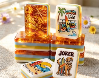 May include: A collection of rectangular mahjong tiles featuring amber-colored resin bases with blue and yellow stripes. The tiles display various graphics including a palm tree, a surfboard with the text Venice, a beach scene, and a dog with a surfboard labeled Joker.