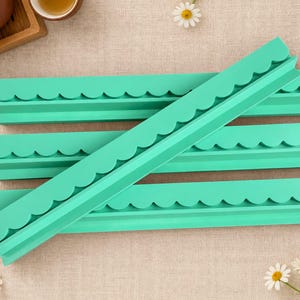 May include: Four long, mint green silicone molds with a scalloped edge design. The molds are rectangular and feature a continuous curved pattern along one side, designed for creating decorative borders or trim elements in crafting projects.