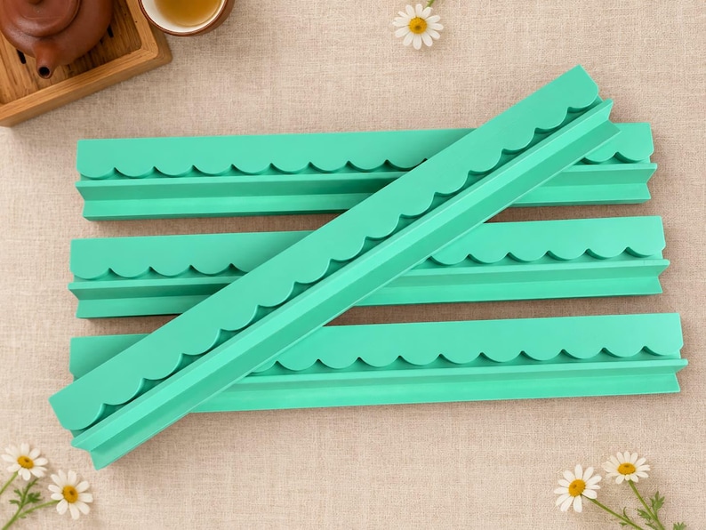 May include: Four long, mint green silicone molds with a scalloped edge design. The molds are rectangular and feature a continuous curved pattern along one side, designed for creating decorative borders or trim elements in crafting projects.