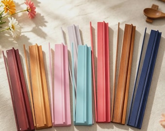 Puede incluir: Una colección de soportes de exhibición rectangulares de madera en varios colores, incluyendo rojo oscuro, madera clara, rosa, azul claro, rojo, madera media y azul oscuro. Cada soporte cuenta con una ranura central para sostener objetos.