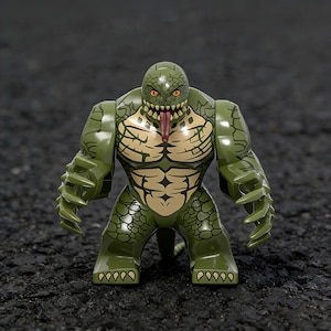 Puede incluir: Figura de acción verde de un humanoide reptiliano con un diseño texturizado detallado. La figura tiene un torso bronceado con definición muscular, una larga lengua roja y ojos anaranjados.