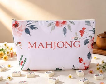 May include: A white zippered pouch featuring a floral pattern with pink and red flowers and green leaves. The word MAHJONG is printed in large, centered, red capital letters. The pouch is surrounded by scattered white mahjong tiles.