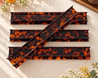May include: Three rectangular wall-mounted shelves featuring a glossy brown and black tortoiseshell pattern. Each shelf has a flat base and a raised back edge, with small circular mounting holes visible along the top horizontal surface.