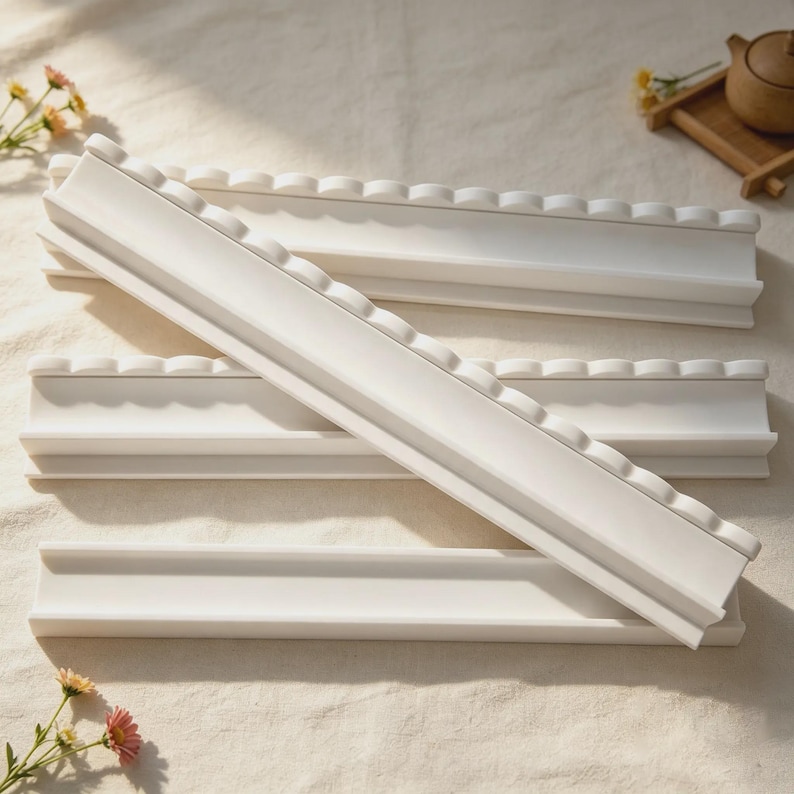 May include: A set of four white, rectangular, elongated trays with a scalloped top edge. Each tray features a smooth, matte finish and a central channel, designed for holding items. The pieces are arranged in a stacked, overlapping formation.