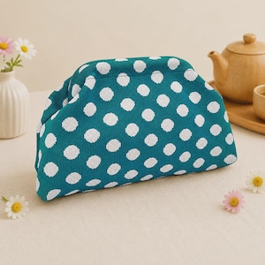 May include: A teal pouch with a white polka dot pattern featuring a structured frame closure. The exterior has a textured knit appearance, and the design is consistent across the front panel of the accessory, which is shaped with rounded corners.