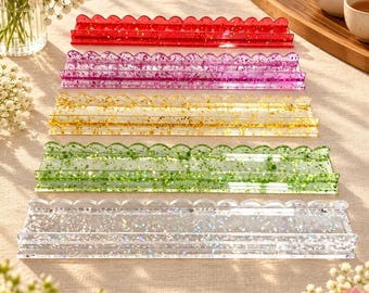 May include: Five rectangular resin display stands with scalloped top edges, arranged in a vertical row. Each stand features a different color embedded with metallic flakes: red, purple, gold, green, and a clear base with iridescent glitter.