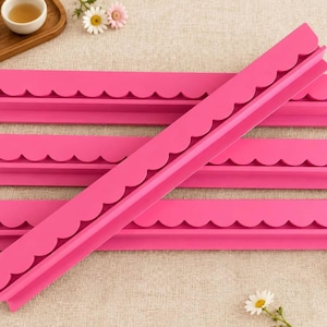 May include: Four bright pink silicone molds, each featuring a long, straight edge with a repeating scalloped pattern along one side. The molds are rectangular in shape and are arranged in a stacked formation with one piece placed diagonally across the others.