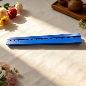 May include: A long, rectangular blue wooden wall shelf featuring a decorative scalloped edge along the front. The shelf has a flat top surface and a grooved design, finished in a solid, vibrant blue paint with a visible wood grain texture.