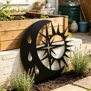 May include: A matte black metal wall art piece featuring a crescent moon shape integrated with a sunburst design. The moon portion includes several teardrop-shaped cutouts, while the sun portion displays sharp, radiating points.
