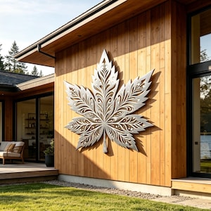 May include: A large, silver-colored metal wall art piece shaped like a maple leaf with intricate, laser-cut filigree patterns and small star cutouts, mounted on the exterior vertical wood siding of a modern house.