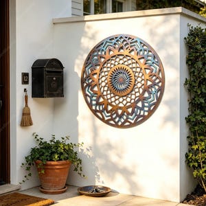 May include: A circular wall art piece with a copper and teal patina finish featuring an intricate geometric mandala pattern. The design includes a central sunburst motif surrounded by concentric layers of repeating petal and lattice shapes.