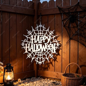 Könnte beinhalten: Ein weißes, kreisförmiges, lasergeschnittenes Schild mit Spinnennetzmuster und dem Text "HAPPY HALLOWEEN" in der Mitte. Das Schild hängt an einem Holzzaun, begleitet von einer schwarzen Laterne und einem geflochtenen Korb.