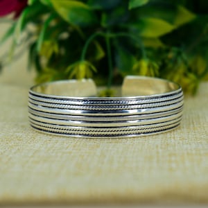 May include: Silver cuff bracelet with a series of horizontal textured bands. The bracelet has a polished finish and a simple, elegant design. The cuff is approximately 2.5 inches in diameter.