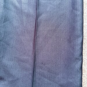May include: Close-up of navy blue fabric with a subtle herringbone pattern. The fabric has a slight sheen and a vertical seam is visible. The texture appears smooth and the color is a deep, solid blue.