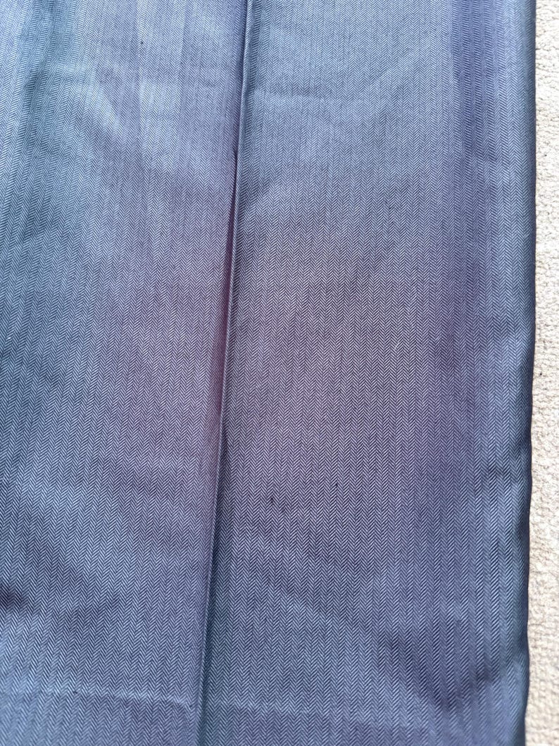 May include: Close-up of navy blue fabric with a subtle herringbone pattern. The fabric has a slight sheen and a vertical seam is visible. The texture appears smooth and the color is a deep, solid blue.