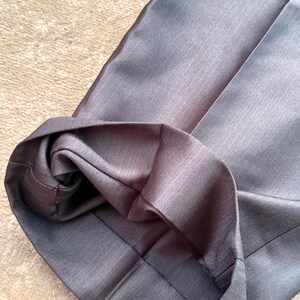 May include: Close-up of a pair of gray dress pants with a folded hem. The fabric has a subtle herringbone pattern. The pants are made of a smooth, possibly synthetic material.