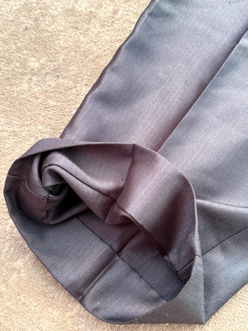 May include: Close-up of a pair of gray dress pants with a folded hem. The fabric has a subtle herringbone pattern. The pants are made of a smooth, possibly synthetic material.