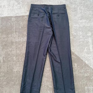 May include: Dark gray dress pants with two back pockets and button closures. The pants are made of a smooth fabric and have a classic, tailored design. The pants are laid flat on a light gray surface.