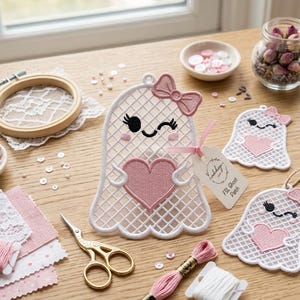 May include: Three white freestanding lace ghost ornaments with pink embroidered hearts and bows. The largest ghost features a small beige tag with the text FSL Ghost Patch. The ghosts have black stitched eyes and pink cheeks, with a grid-like structure.