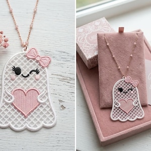 May include: A necklace featuring a white embroidered ghost pendant with a pink heart, a pink bow, and a winking face. The pendant hangs from a delicate rose gold chain with small beads. The text "GHOSTY LOVE" is printed on a small card nearby.