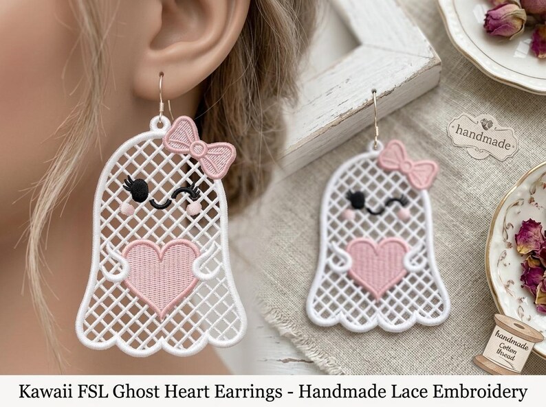 May include: A pair of white ghost-shaped earrings featuring a lattice pattern, a pink embroidered heart, and a small pink bow. The ghost has black embroidered eyes with eyelashes and pink cheeks. Each earring hangs from a silver-toned metal hook.