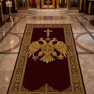 Op de afbeelding: Een bordeauxrode rechthoekige vloerkleed met een gouden rand en een gouden dubbelkoppige adelaar embleem. Het vloerkleed bevindt zich in een kerk, met marmeren vloeren en sierlijke gouden armaturen op de achtergrond.