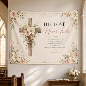 以下が含まれることがあります： 「HIS LOVE Never Fails」のテキストと花のアクセントが入ったクリーム色の壁掛け。木の十字架には花が飾られています。テキストには聖書の詩が含まれています。バナーは金の縁取りとフラワーアレンジメントで縁取られています。