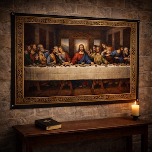 May include: A framed tapestry of the Last Supper scene, featuring Jesus and his disciples. The artwork has a gold and black border and is displayed on a brick wall. A bible and candle are on a wooden table beneath it.