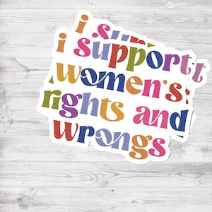 Puede incluir: Una pila de pegatinas blancas con el texto "I support women's rights and wrongs" en varios colores. Sobre un fondo de vetas de madera clara.