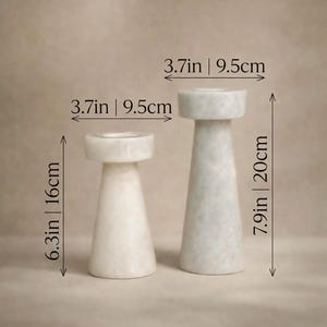 Op de afbeelding: Twee marmeren kandelaars. De kleinere is 16 cm hoog en de grotere 20 cm. Beide zijn 9,5 cm breed. De kandelaars hebben een cilindrische basis en een platte bovenkant. Minimalistisch ontwerp.