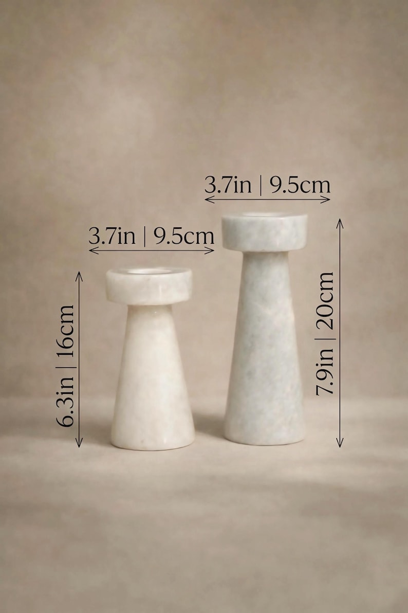 Op de afbeelding: Twee marmeren kandelaars. De kleinere is 16 cm hoog en de grotere 20 cm. Beide zijn 9,5 cm breed. De kandelaars hebben een cilindrische basis en een platte bovenkant. Minimalistisch ontwerp.