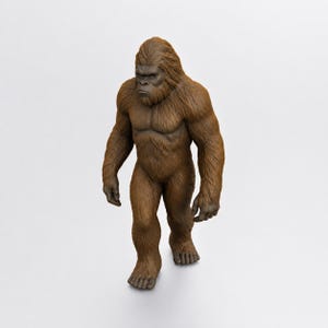 May include: A brown, fur-covered figurine of a bipedal primate standing in a walking pose. The figure features a dark, textured face, defined muscular chest, and long arms reaching toward the ground, captured in a realistic, upright stance.