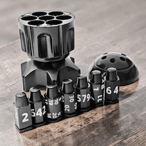 以下が含まれることがあります： 7つの円形コンパートメントを備えた、黒いリボルバー型のデスクオーガナイザー。 白い数字の付いた弾丸型のサイコロと、小さな黒いドーム型の容器が含まれています。 セットは木製の表面に表示されています。