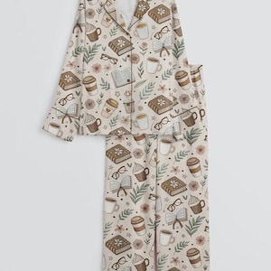 May include: A beige pajama set featuring a repeating pattern of books, coffee cups, eyeglasses, and flowers. The long-sleeved top has a button-down front and a notched collar. The pants are straight-legged.