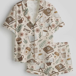 May include: A beige pajama set featuring a pattern of books, coffee cups, eyeglasses, and flowers. The short-sleeved top and shorts have brown trim. The design includes various shades of brown, beige, and green.
