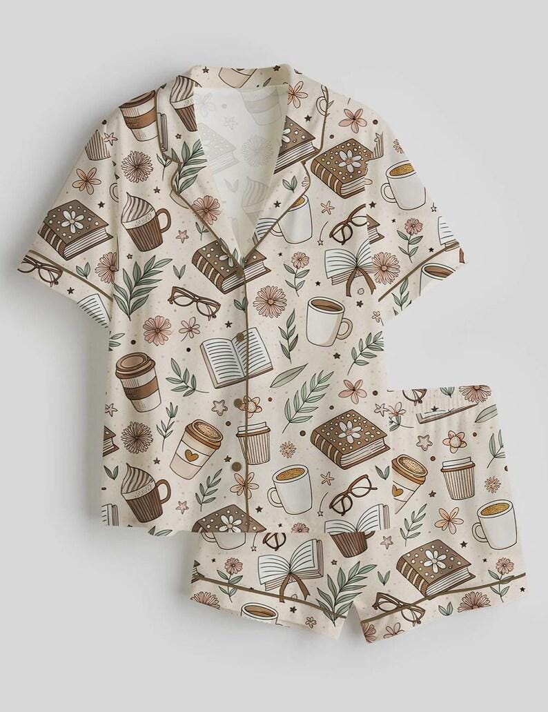 May include: A beige pajama set featuring a pattern of books, coffee cups, eyeglasses, and flowers. The short-sleeved top and shorts have brown trim. The design includes various shades of brown, beige, and green.