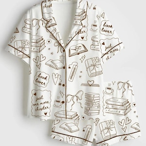 May include: A white short-sleeve button-down pajama set with brown piping and a repeating print of books, coffee cups, bows, hearts, and text that reads "book lover" and "just one more chapter" in a hand-drawn style across the shirt and shorts.