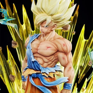 May include: A detailed figurine of a muscular, blonde-haired character in a dynamic pose. The figure wears torn orange and blue clothing, with a determined expression. Yellow energy effects emanate from behind the figure, set against a black background.