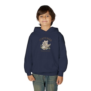 Può includere: Felpa con cappuccio blu navy con grafica di koala e la scritta "AUSTRALIA" sopra. La grafica include un koala e un cucciolo di koala su un ramo. Il testo "The Land Down Under" è sotto. La felpa è indossata da un bambino.