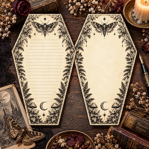 May include: Two coffin-shaped stationery sheets with cream-colored paper. Each features a black ink illustration of a moth with a skull pattern, ferns, mushrooms, and a crescent moon. One sheet has horizontal lines, while the other is blank.